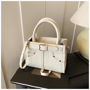 Gros plan d'un sac bandoulière crème avec boucle décorative et détails de rivets