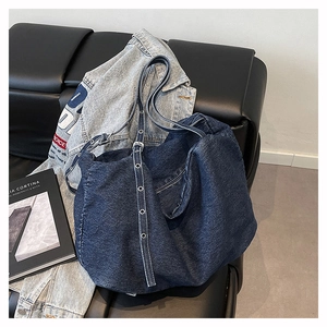 Detail of dark blue denim tote bag with adjustable metal eyelet strap on leather background