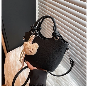 Close-up of black lychee-textured bucket bag with plush bear charm and silk scarf detail
