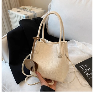 Détail d'un sac seau en cuir blanc cassé avec pendentif éléphant sur fond de décor urbain