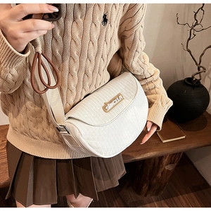 Detail of white quilted half-moon saddle bag with wide strap and gold logo lettering