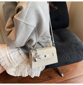 Creamy white textured Kelly bag detail featuring silver twist lock and dog pendant charm