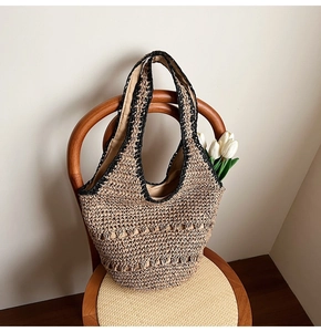 Detail of hand-woven straw hobo bag with black crochet trim on a wooden chair
