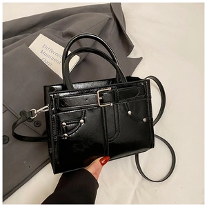 Détails du sac à bandoulière noir brillant avec rivets argentés posé sur un costume gris