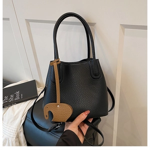 Détail du sac seau en cuir grainé noir avec charme éléphant marron et bandoulière longue