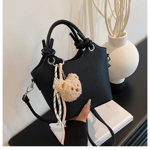 Close-up of black lychee grain texture bucket bag with knotted handle and plush bear charm