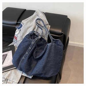 Detail of blue denim hobo bag with metal eyelets on shoulder strap over black sofa