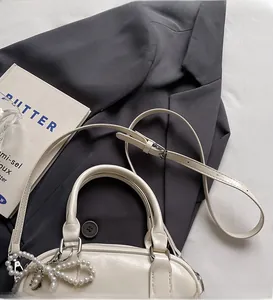 Detail of cream leather handbag showing long adjustable strap and pearl charm accessory