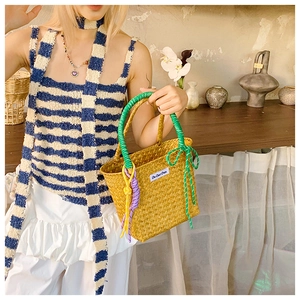 Detail of straw bucket bag featuring green handles and colorful decorative cords