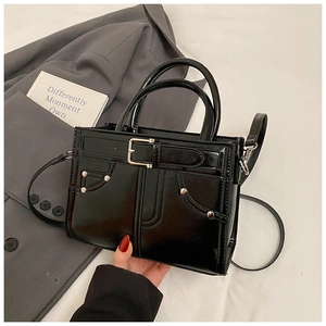 Détail d'un sac à main noir brillant avec boucle décorative et rivets métalliques élégants