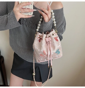 Détail du sac seau en satin rose avec broderie papillon et poignée en perles