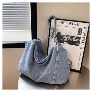 Close-up of light blue denim tote bag with metal rivet details and washed texture