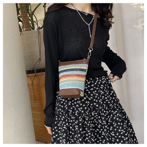 Detail of colorful striped woven crossbody bag with brown faux leather trim and strap