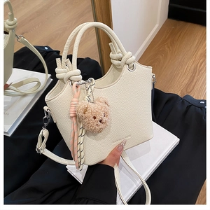 Detail of cream pebbled leather bucket bag with knot handle and teddy bear charm