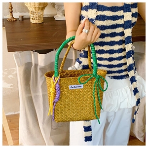 Detailed close-up of a woven straw bucket bag featuring green rope handles and a brand tag