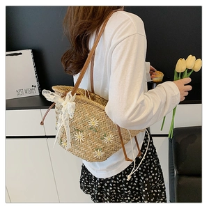 Detail of straw bucket bag featuring white daisy embroidery and lace bow on shoulder strap
