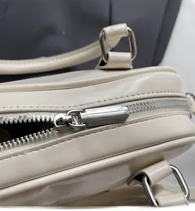 Close-up of smooth silver metal zipper and stitching on the cream-colored handbag