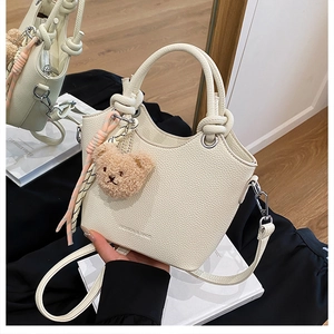 Close-up of beige bucket bag showing lychee leather texture and plush bear charm accessory