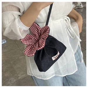 Detail of blue denim bucket bag with red checkered floral trim and shoulder strap