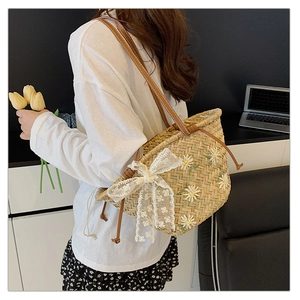 Detail of straw tote bag featuring daisy embroidery, lace bow, and brown leather handles