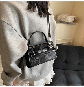 Detail of black glossy crinkled leather bag with silver twist lock and charm