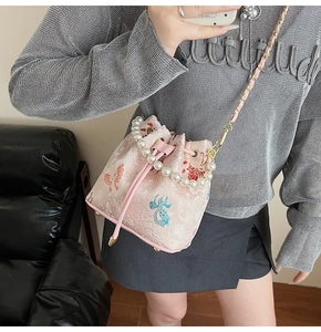 Detail of pink embroidered bucket bag with pearl handle and golden chain strap