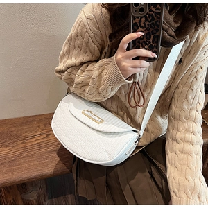 Close-up of white saddle bag with wavy quilting and gold hardware on wide strap