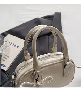 Detail of creamy white handbag with glossy leather finish and pearl charm accessory