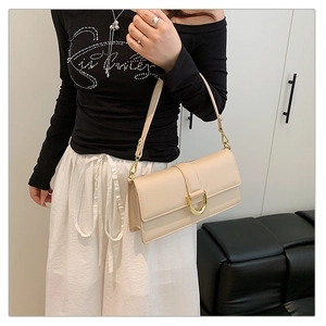 Détail d'un sac baguette en cuir beige crème avec boucle dorée en D porté par un mannequin