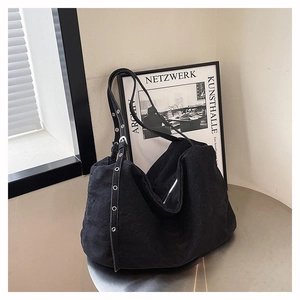 Detail of black canvas tote bag showing silver grommet shoulder strap on metal surface
