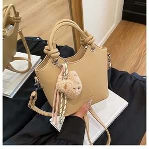 Close-up of beige textured leather bucket bag with knot handle and cute bear charm
