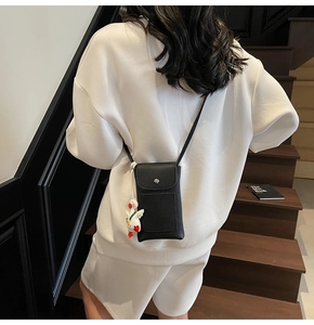 Detail of black pebbled leather crossbody phone bag with a cute white goose pendant