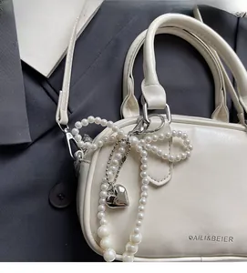 Detail of cream white leather handbag with large pearl bow and heart charm
