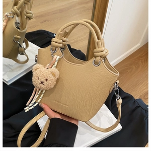 Close-up of khaki bucket bag with lychee texture, knot handle and plush bear charm