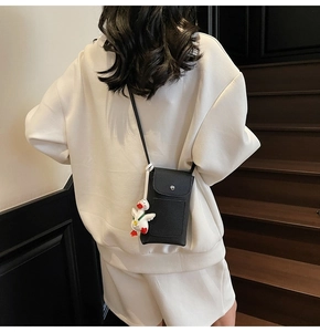 Detailed view of a black lychee texture leather crossbody phone bag with a cute duck charm