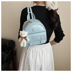 Detail of light blue mini backpack with plush bear charm and embossed logo on front pocket