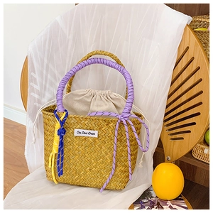 Detail of straw woven bucket bag with purple rope handle and colorful knotted accents
