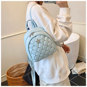 Detail of light blue quilted mini backpack with metal studs and star emblem on model