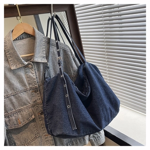 Detail of dark blue denim tote bag featuring adjustable silver metal eyelet straps