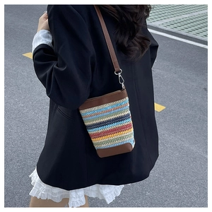 Detail of colorful rainbow woven straw crossbody bag with brown leather trim on a model