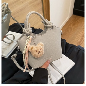 Close-up of grey litchi leather bucket bag with knotted handles and a cute bear charm