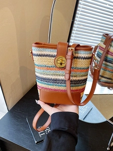 Striped woven bucket bag with brown leather trim and metallic clasp for summer travel