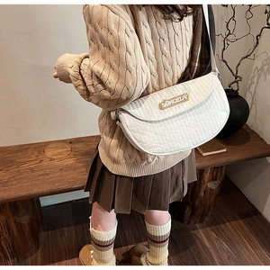 Macro detail of white quilted texture and brand patch on large crossbody saddle bag