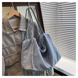 Detail of light blue washed denim tote bag with adjustable strap on denim jacket background