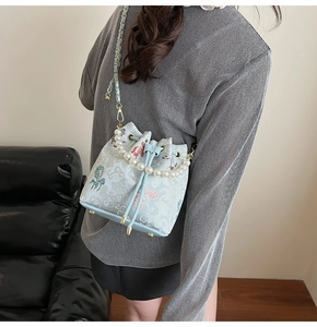 Détail du sac seau brodé bleu clair avec anse en perles porté par un mannequin