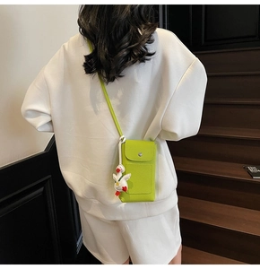 Detail of neon green crossbody phone bag with textured leather and cute duck charm