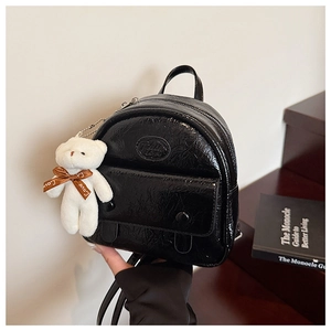 Close-up of black glossy crinkled leather mini backpack with cute plush bear charm