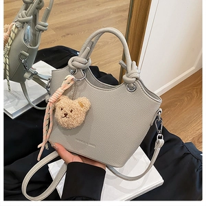 Detail of grey pebbled leather bucket bag with knotted handle and plush bear charm