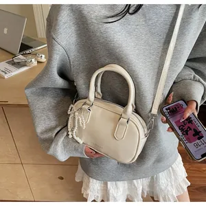 Detail of cream white leather boston bag featuring a pearl bow charm on a wooden desk