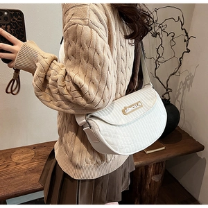 Close-up of white quilted saddle bag with SMKCELA metal logo and vertical stitching